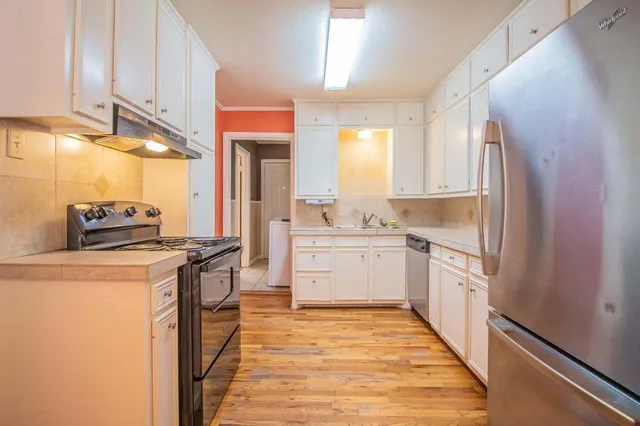 a kitchen with stainless steel appliances a refrigerator a sink and white cabinets