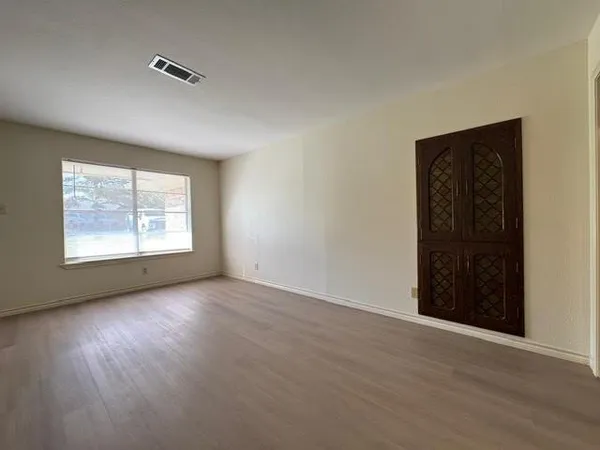 an empty room with wooden floor cabinet and windows