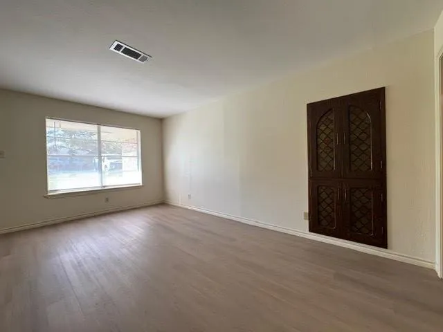 an empty room with wooden floor cabinet and windows