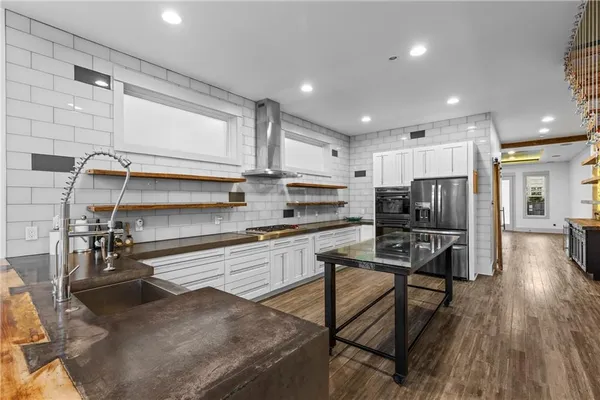a kitchen with stainless steel appliances a refrigerator a sink a stove top oven a dining table and chairs with wooden floor