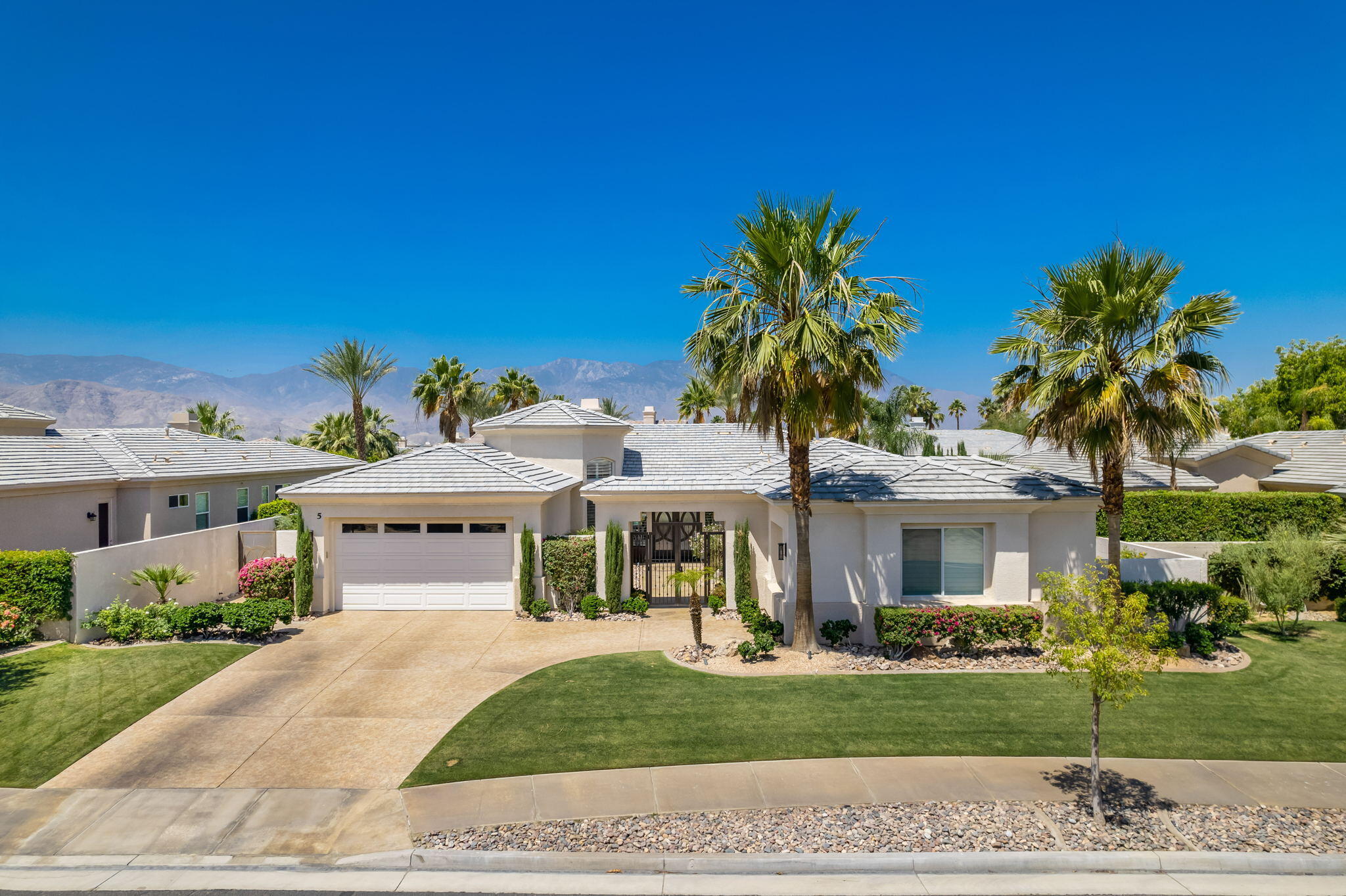 5 Lyon Road Rancho Mirage, CA 92270 - Photo 2 of 50 a view of a white house with a yard and table and chairs under an umbrella