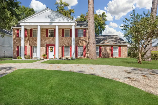 a view of a brick house with a yard and large trees