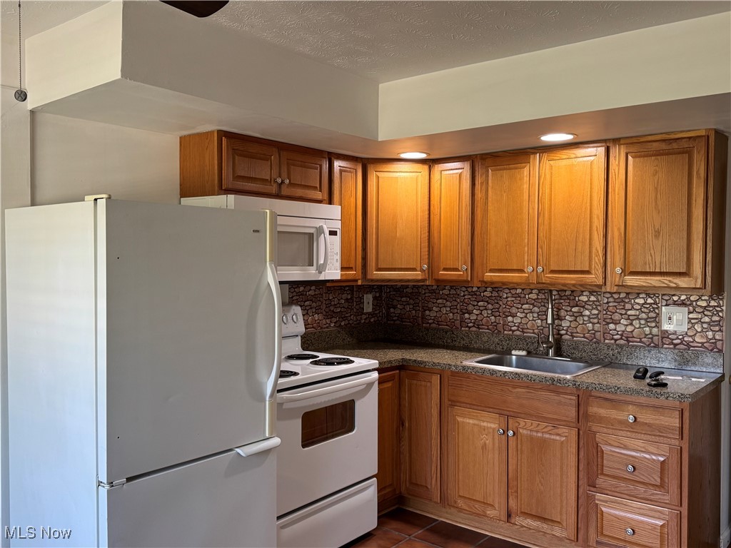 8961 Herbert Road Canfield, OH 44406 - Photo 18 of 26 Kitchen featuring brown cabinets, backsplash, a sink, and white appliances