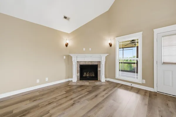 a view of an empty room with wooden floor fireplace and a window