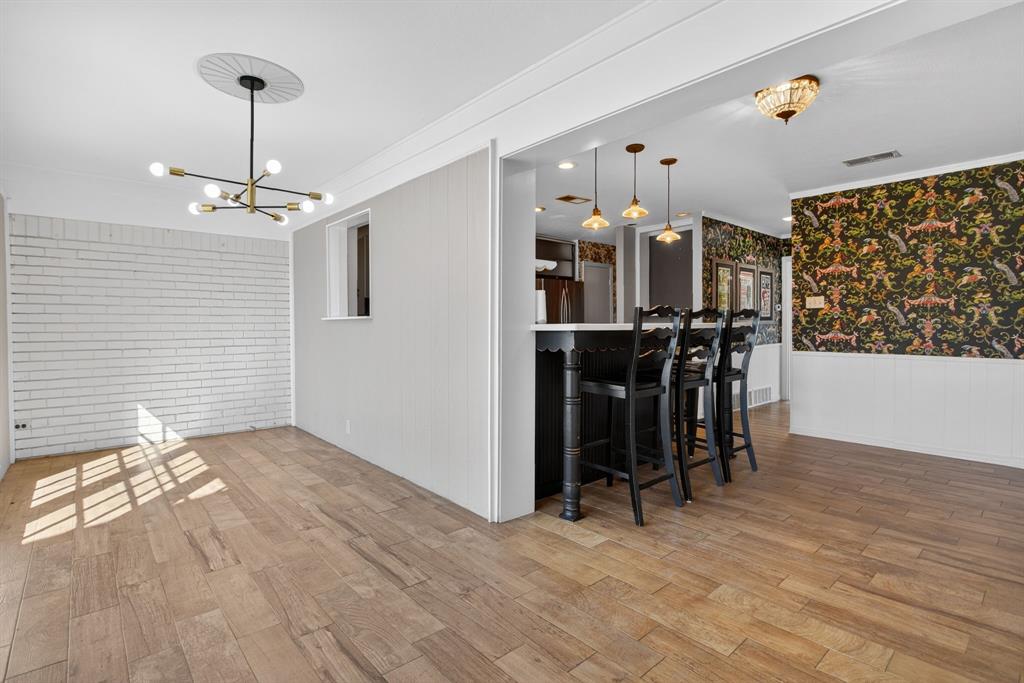 7117 Serrano Drive Benbrook, TX 76126 - Photo 12 of 26 Dining area featuring wood finished floors, a chandelier, wallpapered walls, ornamental molding, and a wainscoted wall