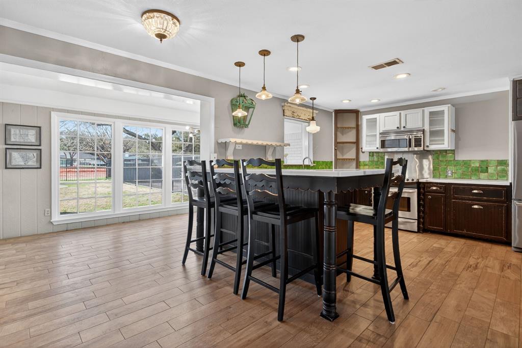7117 Serrano Drive Benbrook, TX 76126 - Photo 13 of 26 Dual tone kitchen featuring a kitchen bar, decorative light fixtures, glass insert cabinets, backsplash, and light wood finished floors