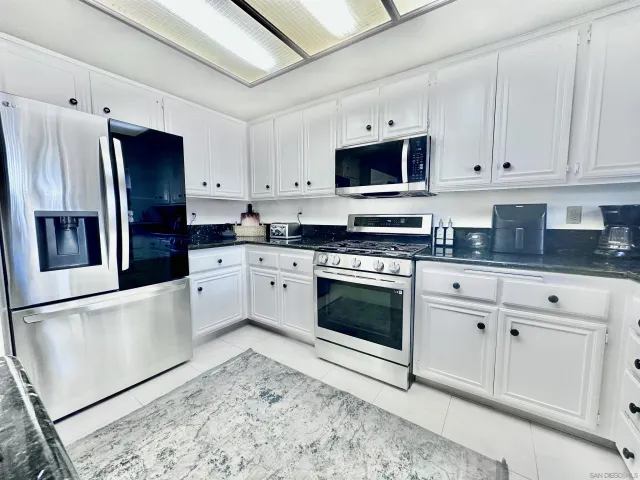 a kitchen with stainless steel appliances granite countertop a refrigerator sink stove and white cabinets