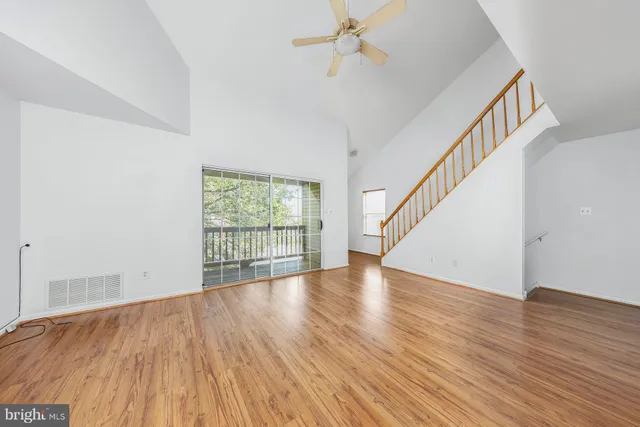 a view of an empty room with wooden floor and fan