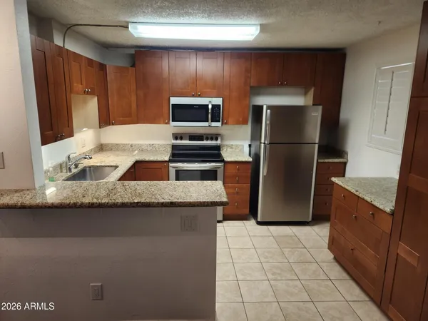 a kitchen with granite countertop wooden cabinets a refrigerator and a stove top oven