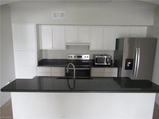 a kitchen with stainless steel appliances granite countertop a sink a stove a refrigerator and white cabinets