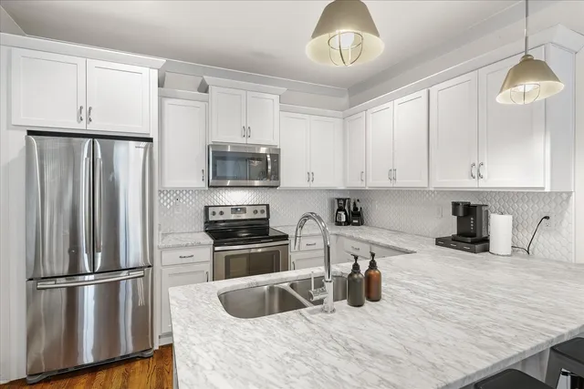 a kitchen with granite countertop a refrigerator a sink a stove and white cabinets