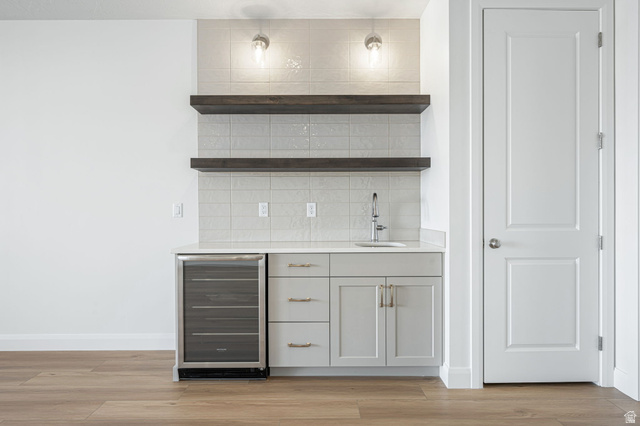 684 West High Tide Place, Unit 131 St. George, UT 84790 - Photo 17 of 27 Built-in wet bar featuring light grey cabinetry, a stainless steel sink with a chrome faucet, a beverage refrigerator, and open wood shelving