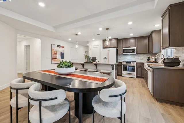 a kitchen with stainless steel appliances kitchen island granite countertop a dining table chairs and a refrigerator