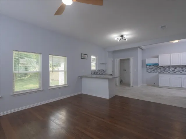 a view of an empty room with wooden floor and a kitchen