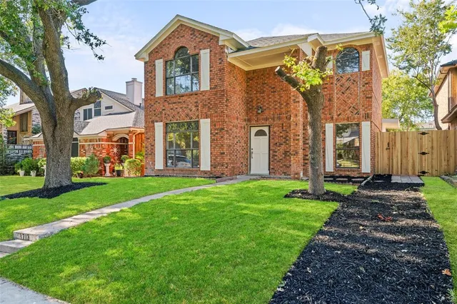a view of a brick house with a large windows and a yard with plants and large tree
