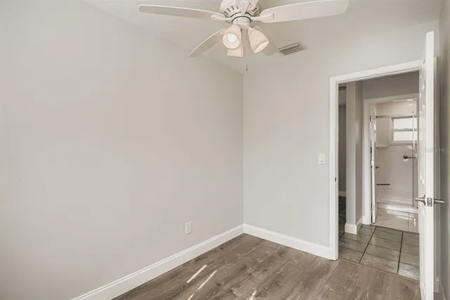 an empty room with wooden floor fan and windows
