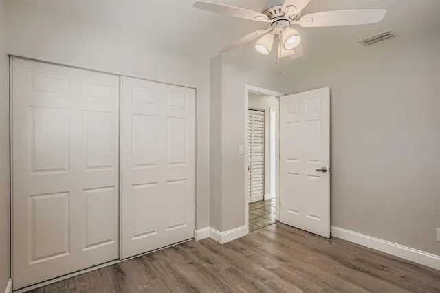 an empty room with wooden floor closet fan and windows
