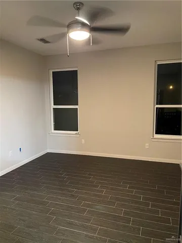 an empty room with wooden floor chandelier fan and windows