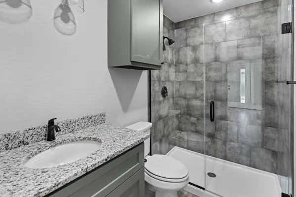 a bathroom with a granite countertop sink a toilet and shower