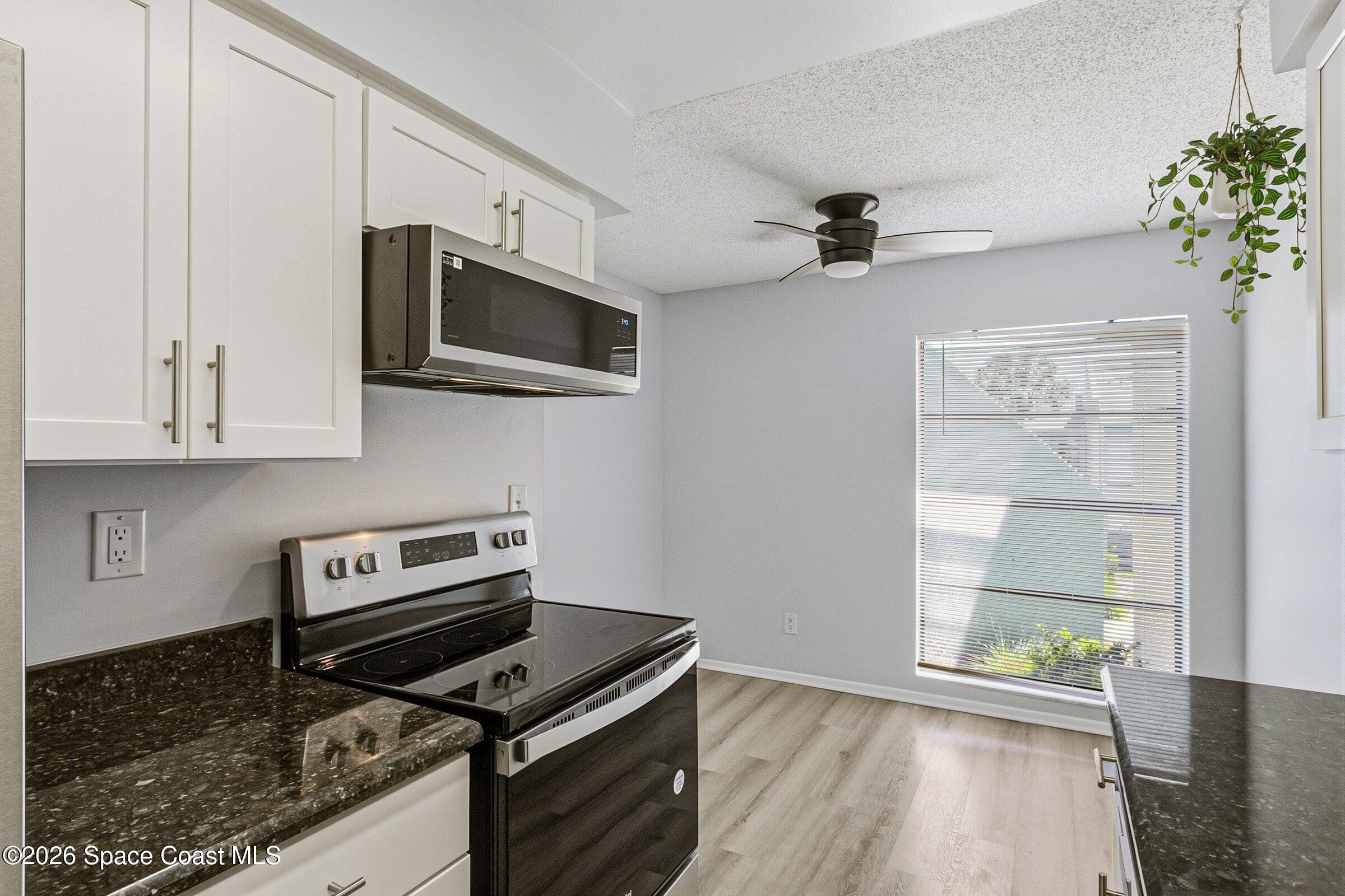 1225 North Wickham Road, Unit 223 Melbourne, FL 32935 - Photo 10 of 26 a kitchen with granite countertop a stove a microwave and wooden floor