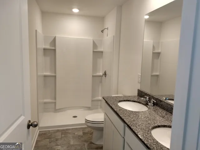 a bathroom with a granite countertop sink a toilet a mirror and shower