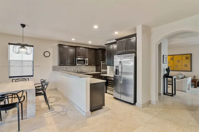 a kitchen with stainless steel appliances kitchen island granite countertop a refrigerator oven a sink a dining table and chairs with wooden floor
