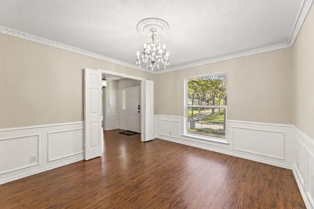 an empty room with wooden floor chandelier and windows