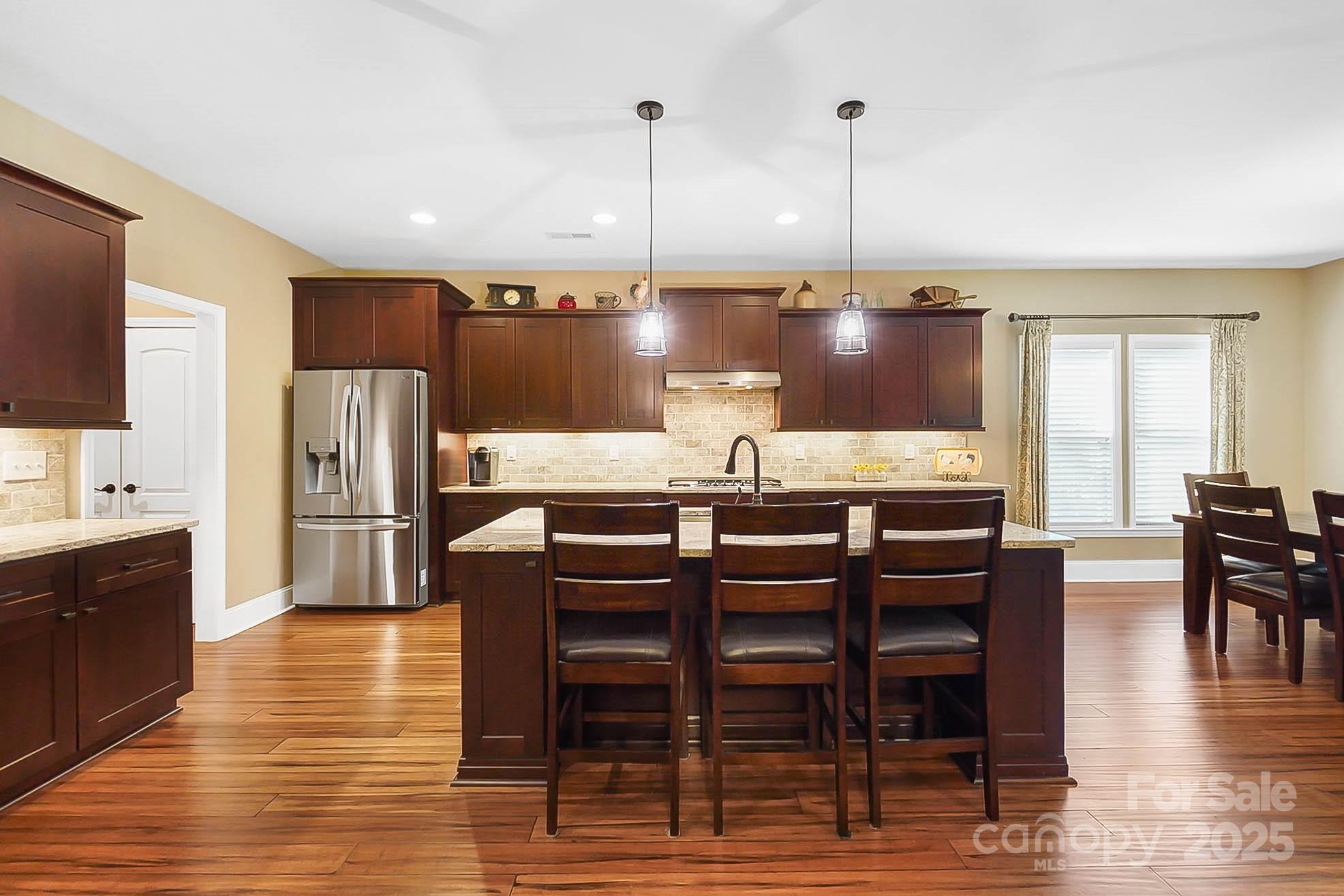 7305 Indian Trail Fairview Road Indian Trail, NC 28079 - Photo 16 of 48 a kitchen with stainless steel appliances kitchen island granite countertop a refrigerator a stove a dining table and chairs with wooden floor