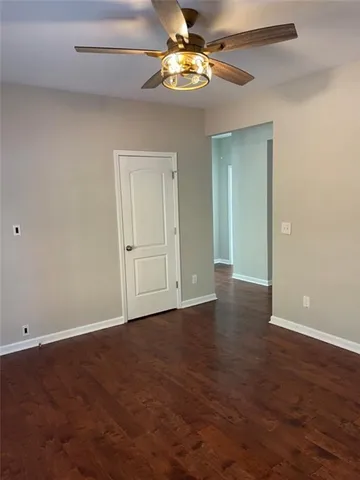 a view of an empty room with chandelier fan and wooden floor