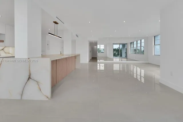 a view of an empty room with kitchen and window