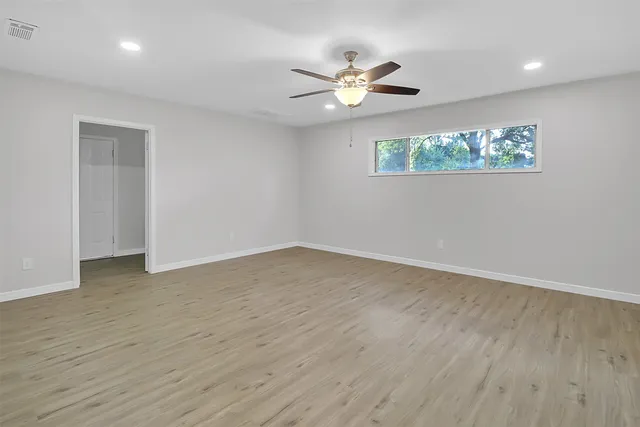 an empty room with wooden floor chandelier fan and windows
