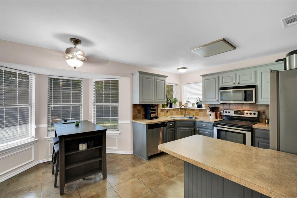 1001 Short Line Boulevard Midlothian, TX 76065 - Photo 4 of 26 Kitchen featuring tile flooring, a bay window with blinds, dual-toned cabinetry, stainless steel appliances, and a built-in kitchen island with a breakfast bar