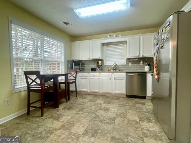 a kitchen with stainless steel appliances a table chairs sink refrigerator and cabinets