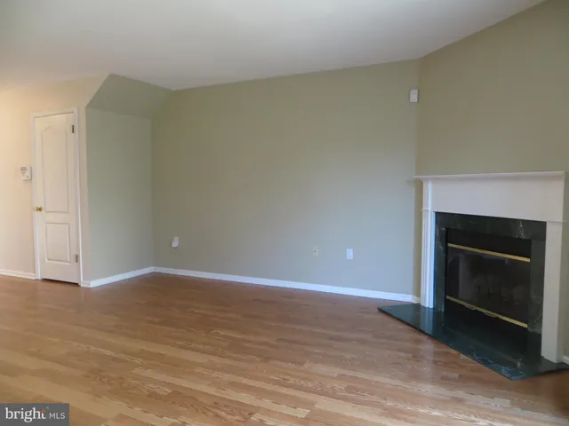 a view of an empty room with wooden floor and a fireplace