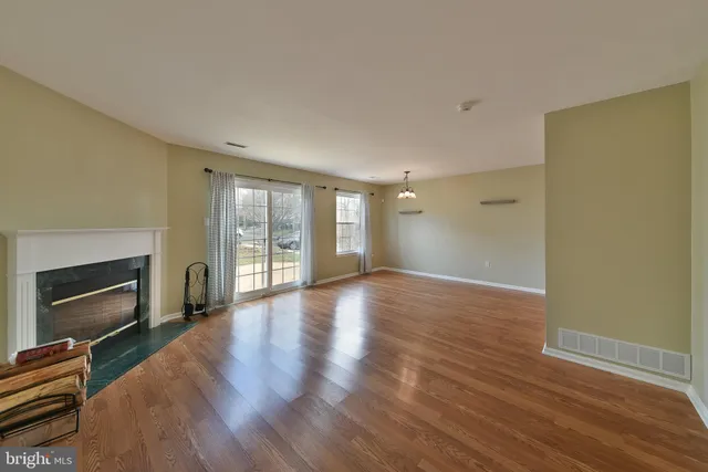 a view of an empty room with wooden floor fireplace and a window