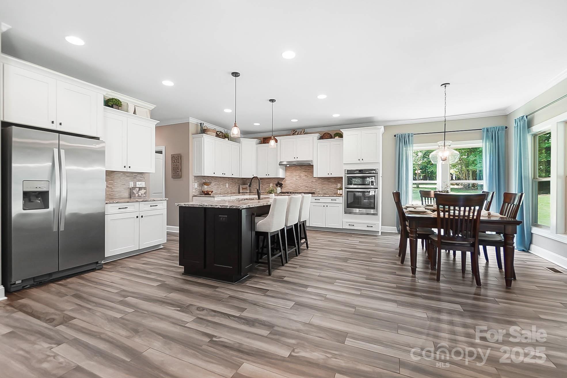 7219 Indian Trail Fairview Road Indian Trail, NC 28079 - Photo 5 of 48 a open kitchen with kitchen island a refrigerator a stove a dining table and chairs with wooden floor