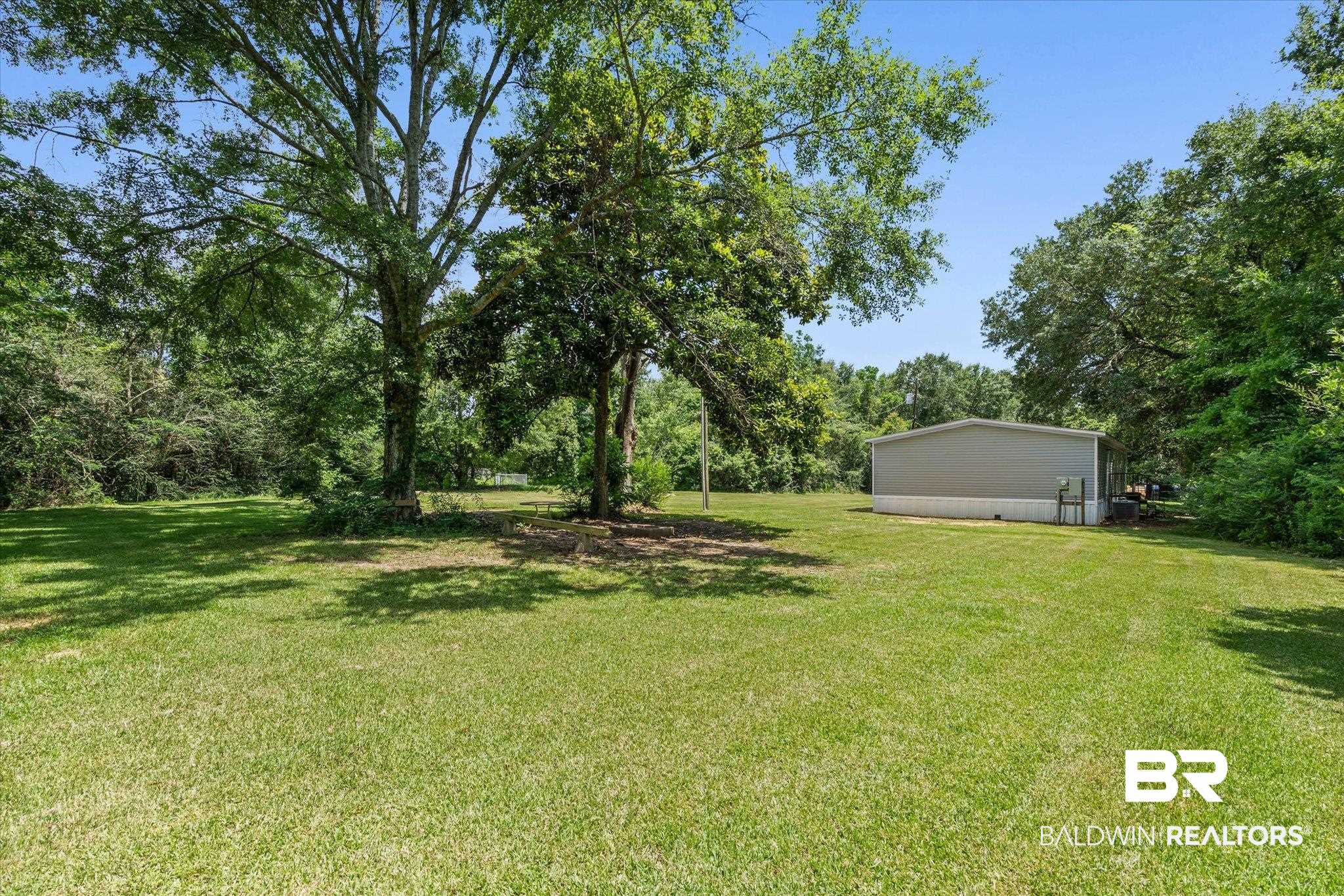 25366 Pollard Road Daphne, AL 36526 - Photo 20 of 22 Expansive green lawn with mature trees and a metal-sided structure featuring a light gray exterior