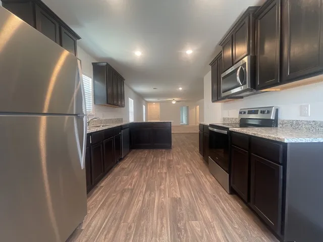 a kitchen with stainless steel appliances granite countertop a refrigerator a sink dishwasher a stove and a microwave oven on dining table