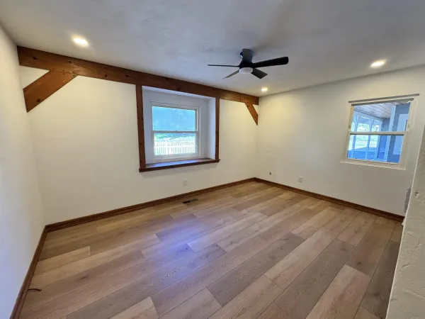 an empty room with wooden floor ceiling fan and windows