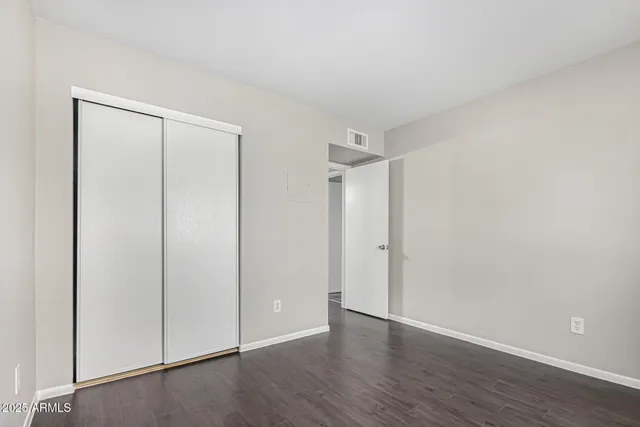 a view of an empty room with wooden floor and closet
