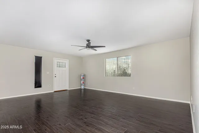 an empty room with wooden floor fan and windows
