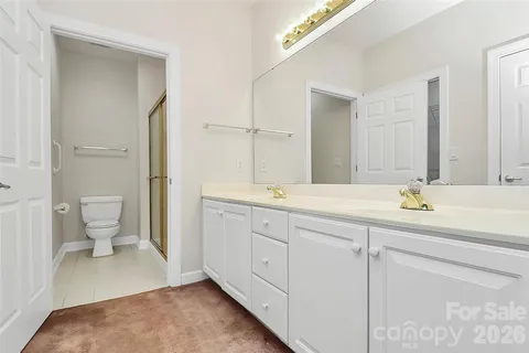 a spacious bathroom with a toilet a double vanity sink and a mirror