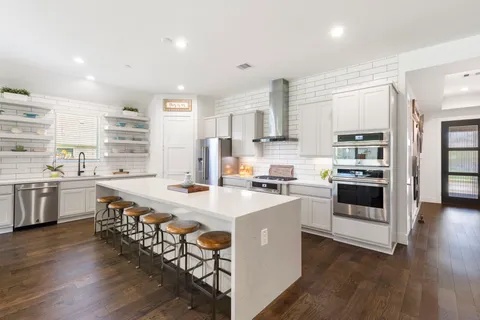 a kitchen with stainless steel appliances a stove a sink dishwasher a refrigerator and white cabinets with wooden floor