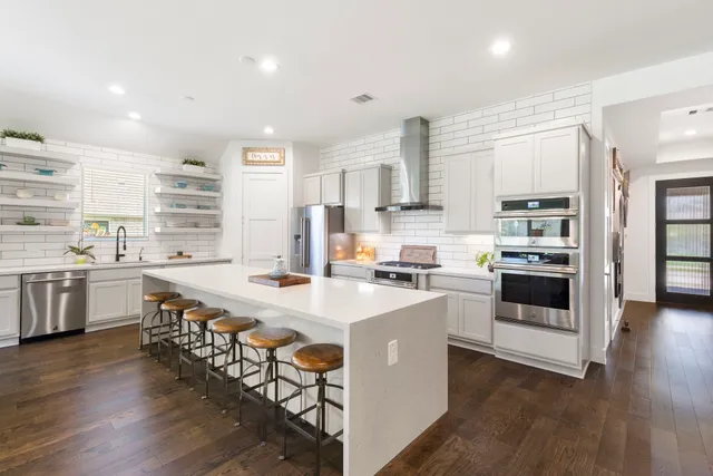 a kitchen with stainless steel appliances a stove a sink dishwasher a refrigerator and white cabinets with wooden floor