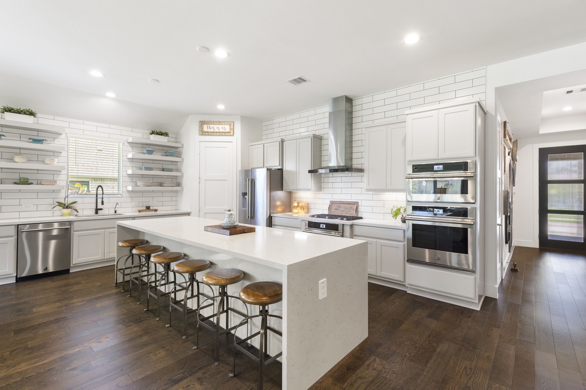 a kitchen with stainless steel appliances a stove a sink dishwasher a refrigerator and white cabinets with wooden floor