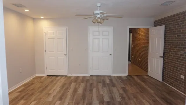 an empty room with wooden floor chandelier fan and windows