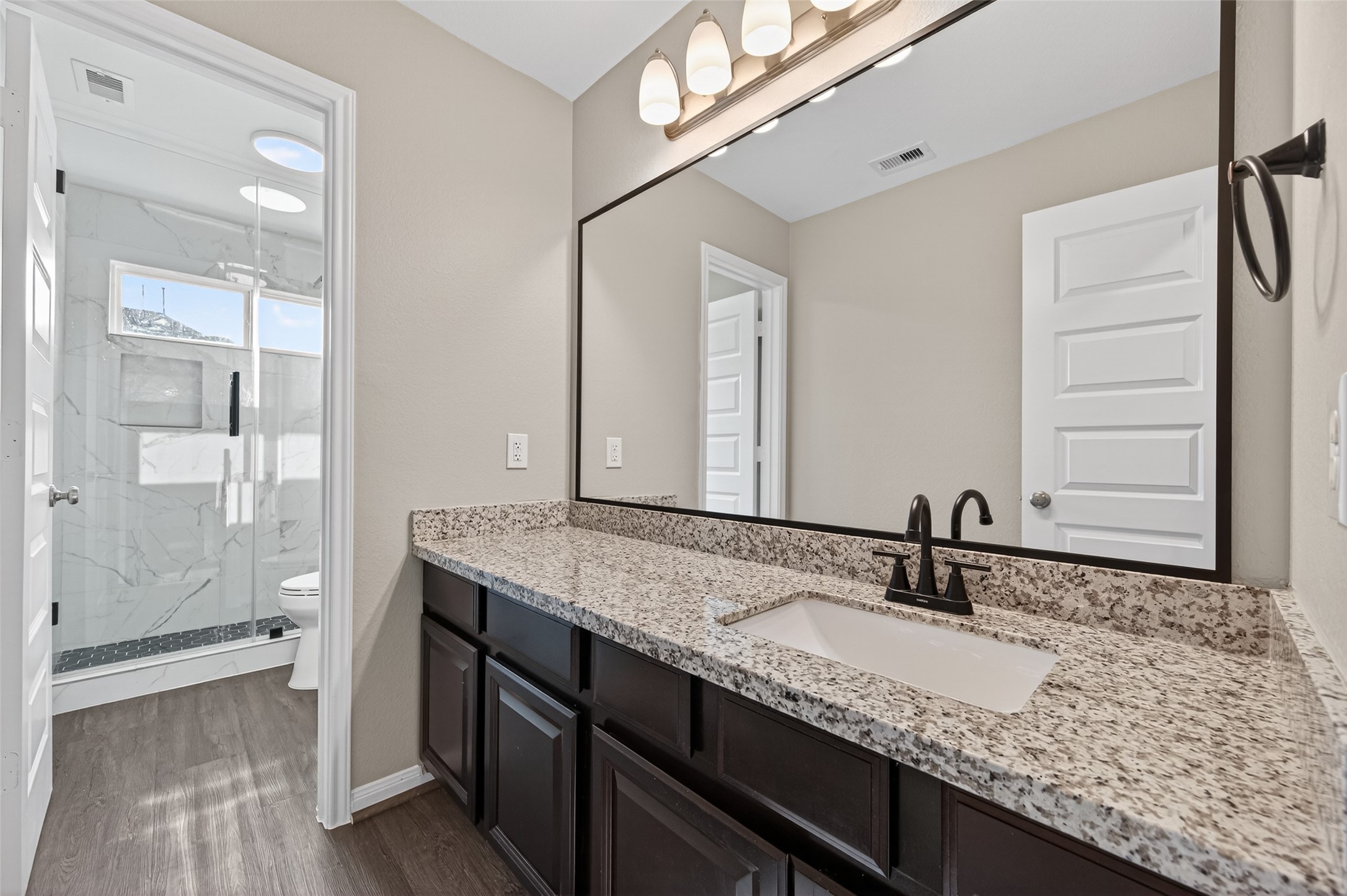 7003 Bristol Memorial Drive Spring, TX 77379 - Photo 32 of 40 Well-appointed upstairs full bathroom conveniently located between the third and fourth secondary bedrooms. This space features a granite vanity with under-mount sink, framed mirror, updated lighting, and rich dark cabinetry for a modern contrast. The separate shower area showcases stylish tilework and glass enclosure, creating a clean, move-in ready feel. Ideal for growing families or guests, this functional and beautifully finished bathroom enhances the smart layout of this spacious Spring TX 77379 home