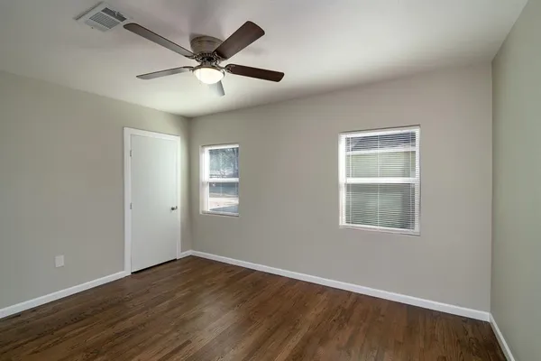 an empty room with wooden floor ceiling fan and windows