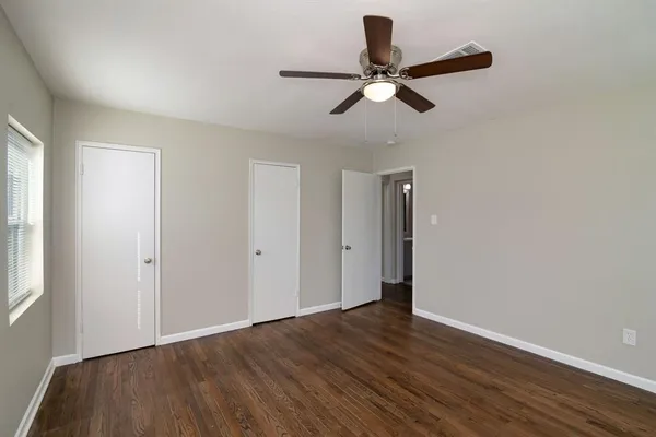 a view of an empty room with wooden floor and a ceiling fan