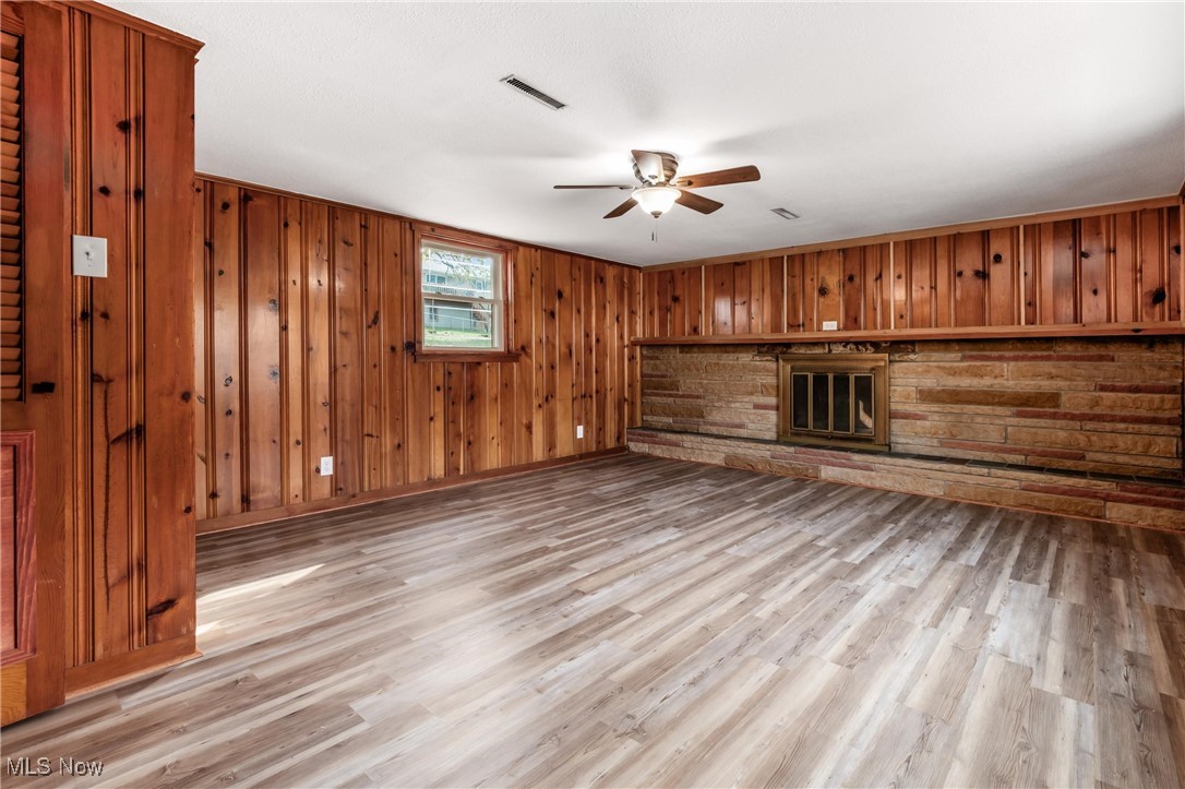 724 Garden Road Zanesville, OH 43701 - Photo 14 of 22 Unfurnished living room featuring light wood-style floors, wood walls, a ceiling fan, and a stone fireplace